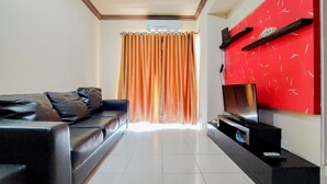 A living room with a black leather sofa, a red accent wall, and a flat-screen TV on a black stand.