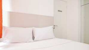 A hotel room with a bed, white bedding, and a door with a handle. - Homey And Strategic 2Br At Bassura City Apartment (Jakarta)