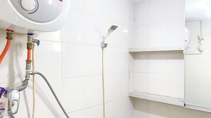 Kylpyhuone, jonka seinät on laatoitettu valkoisilla laatoilla, ja jossa on suihku, jossa on irrotettava suihkupää, sekä wc, jossa putki on näkyvissä.
