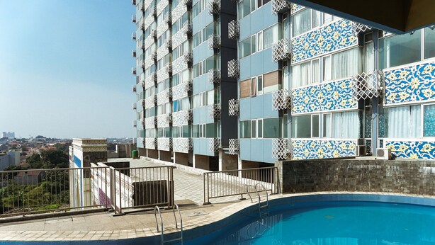 A swimming pool with a view of a high-rise building with patterned windows and balconies. - Comfort Studio At Saladdin Mansion Apartment (Depok)