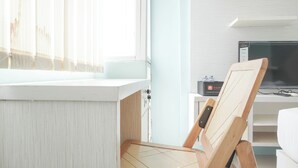 A room with a white cabinet, a wooden chair, a television, and a window with sheer curtains. - Comfort Studio At Saladdin Mansion Apartment (Depok)