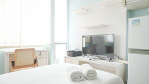 A hotel room with a bed, a desk with a computer, a television, and a refrigerator. - Comfort Studio At Saladdin Mansion Apartment (Depok)