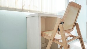 A corner desk with a wooden frame and a glass top, positioned against a light-colored wall near a window with sheer curtains. - Comfort Studio At Saladdin Mansion Apartment (Depok)