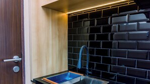 A kitchen with a black tiled backsplash, a stainless steel sink, and a wooden door. - Comfort And High Floor Studio Room At Transpark Bintaro Apartment (South Tangerang)