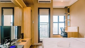 A hotel room with a bed, a desk with a computer, a TV, and a balcony with a view. - Comfort And High Floor Studio Room At Transpark Bintaro Apartment (South Tangerang)
