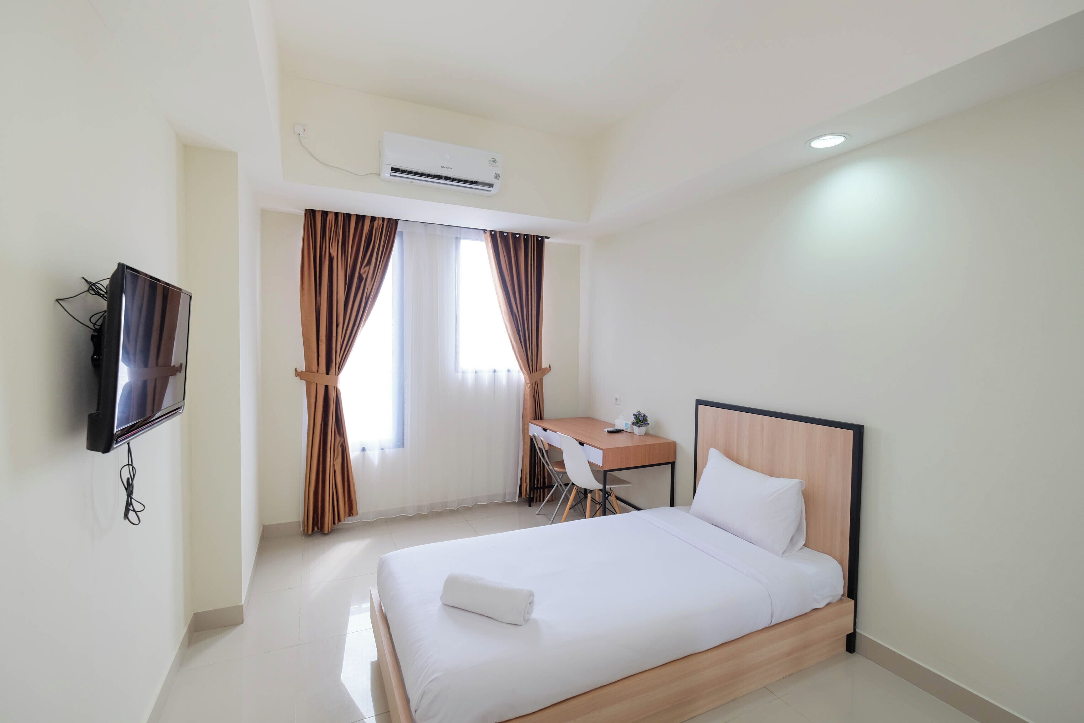 A hotel room with a bed, desk, chair, TV, and air conditioning unit.