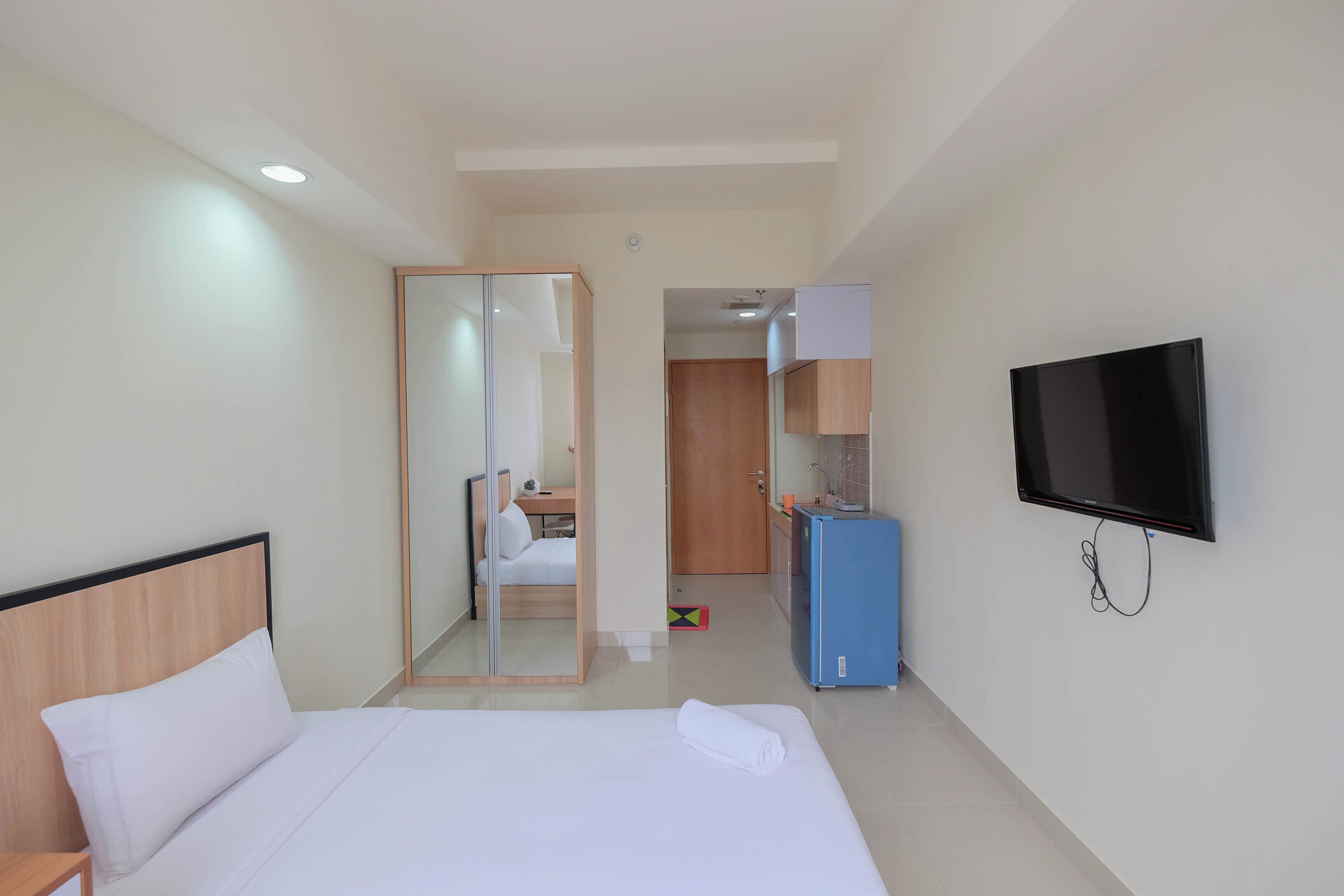 A hotel room with a bed, a television, a wardrobe, and a small kitchenette.