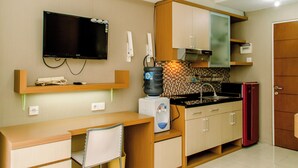 Una cocina compacta con televisión de pantalla plana, dispensador de agua, microondas y refrigerador.