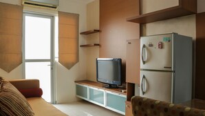 Un ambiente compatto con un divano, una televisione su un mobile, un frigorifero e una porta scorrevole.