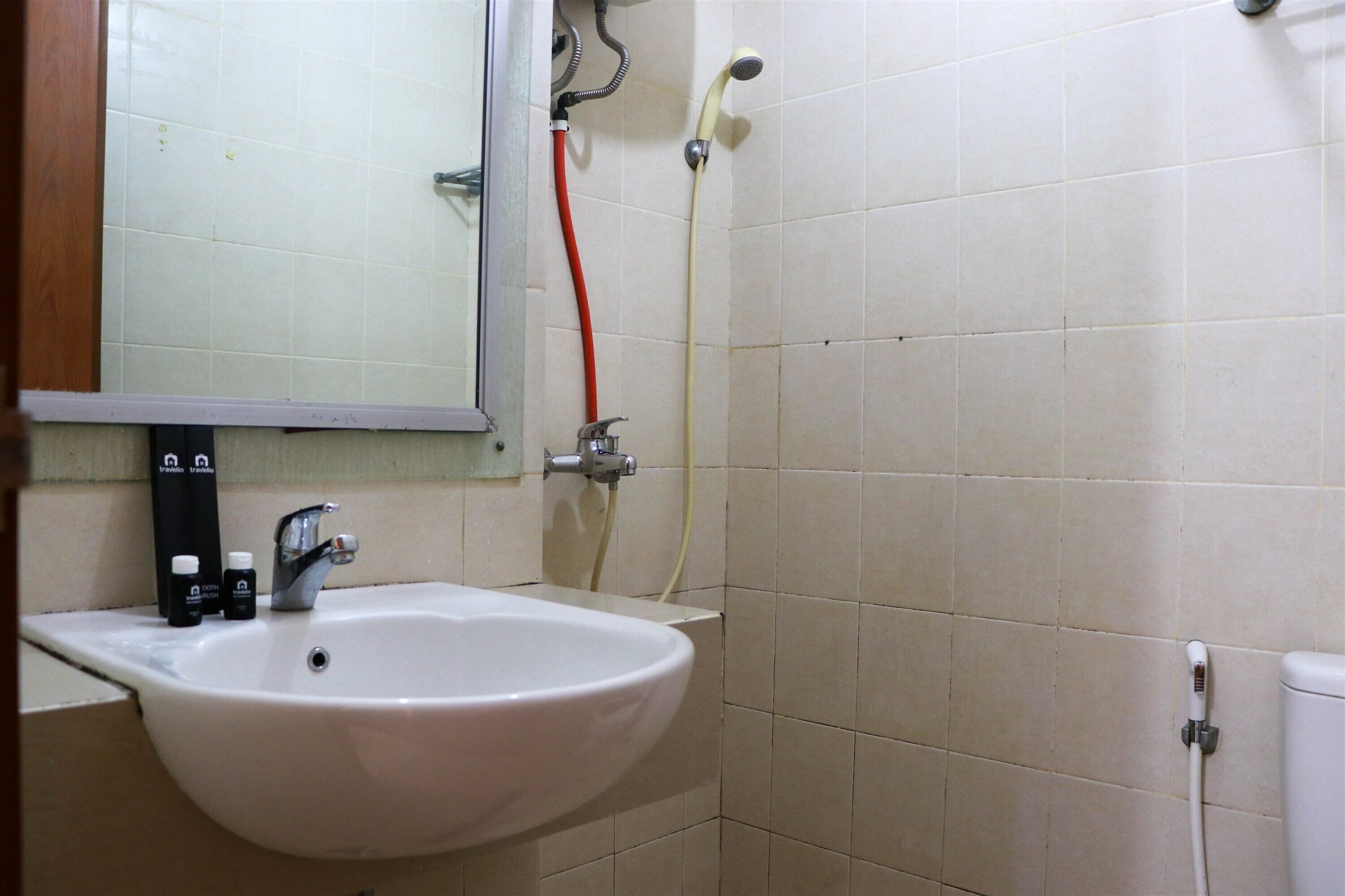A bathroom with a white sink, a mirror, and a shower with a red hose.