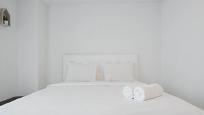 A neatly made bed with white linens and two pillows, a small shelf with a potted plant, and a plain white wall. - Scenic And Comfy Studio West Vista Apartment (Jakarta)