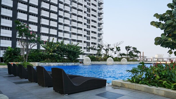 A modern hotel with a rooftop pool, surrounded by lush greenery and a high-rise building in the background. - Scenic And Comfy Studio West Vista Apartment (Jakarta)