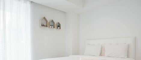 A white bedroom with a large bed, a window with sheer curtains, and three wall-mounted shelves with decorative items.