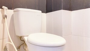 A white toilet with a tank and a seat, connected to a wall-mounted pipe. - Homey And Nice Studio Cinere Bellevue Suites Apartment (Depok)