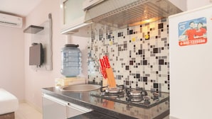 A kitchen with a black countertop, a gas stove, a water dispenser, and a tiled backsplash. - Homey And Nice Studio Cinere Bellevue Suites Apartment (Depok)