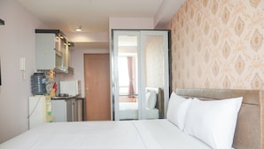 A hotel room with a bed, a kitchenette, and a bathroom visible through an open door. - Homey And Nice Studio Cinere Bellevue Suites Apartment (Depok)