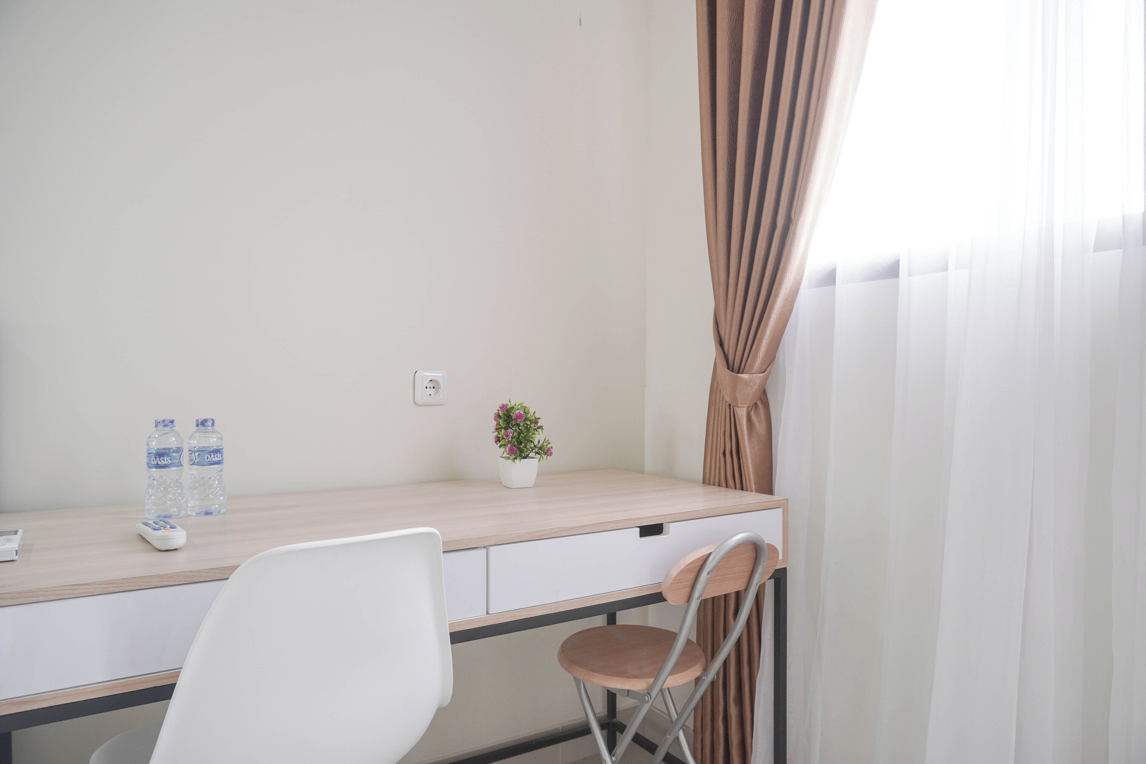 A hotel room with a wooden desk, a white chair, a small potted plant, and two water bottles.