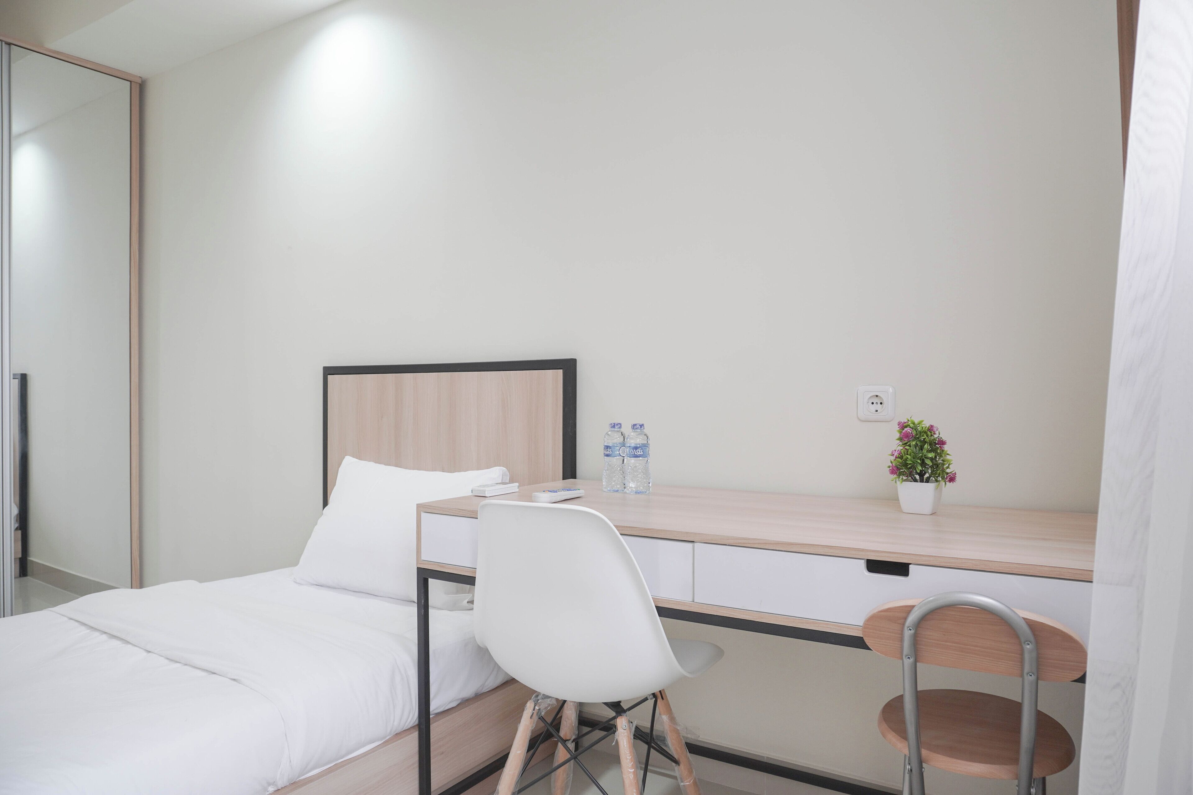 Ein Hotelzimmer mit einem Bett, einem Schreibtisch mit Stuhl, einer Topfpflanze und zwei Wasserflaschen.