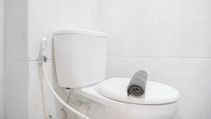 Un waterino bianco con un asciugamano sullo scudo e un porta carta igienica a vista.