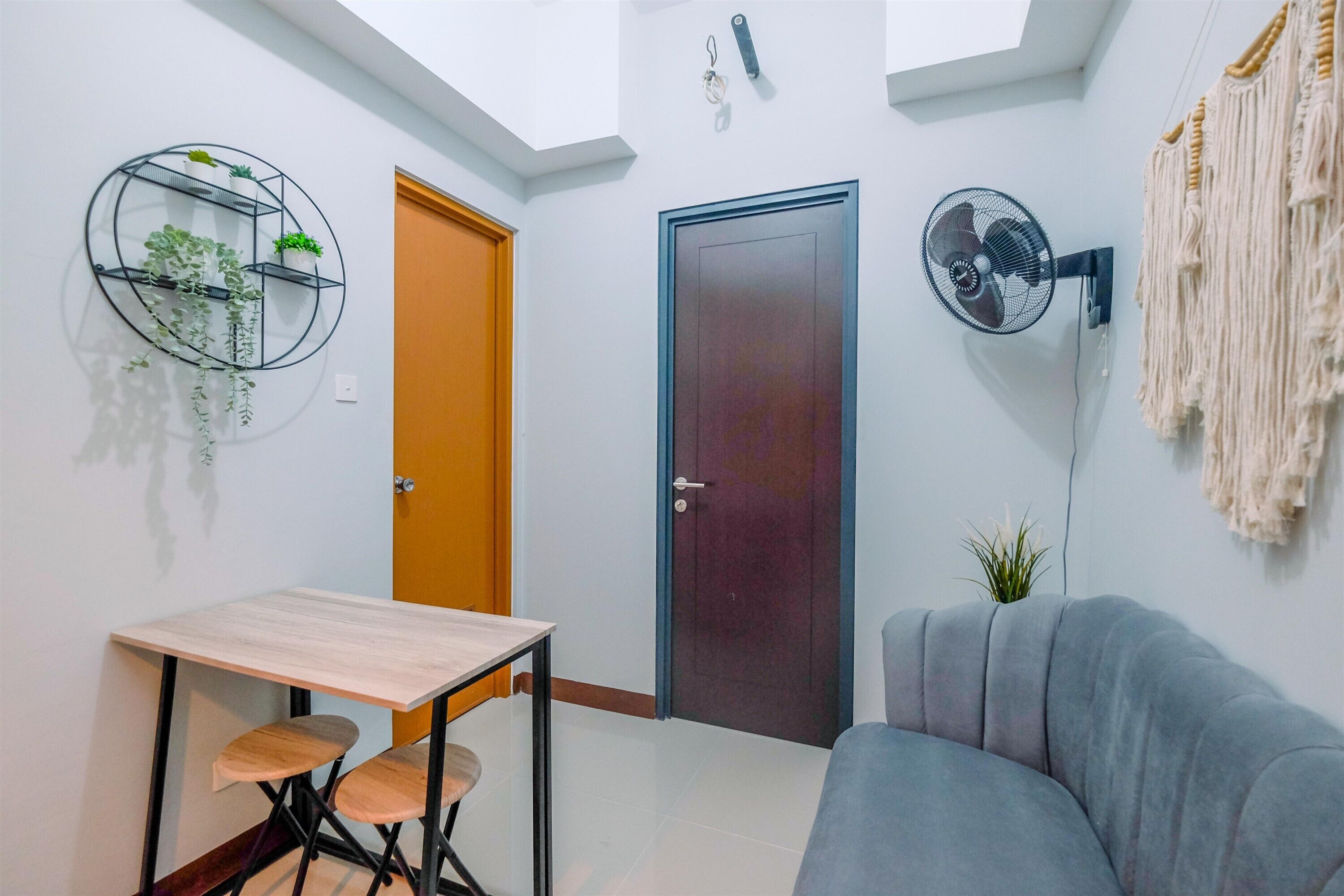 Un espacio habitable compacto con una mesa de comedor, un sofá, un ventilador de pared y una puerta.