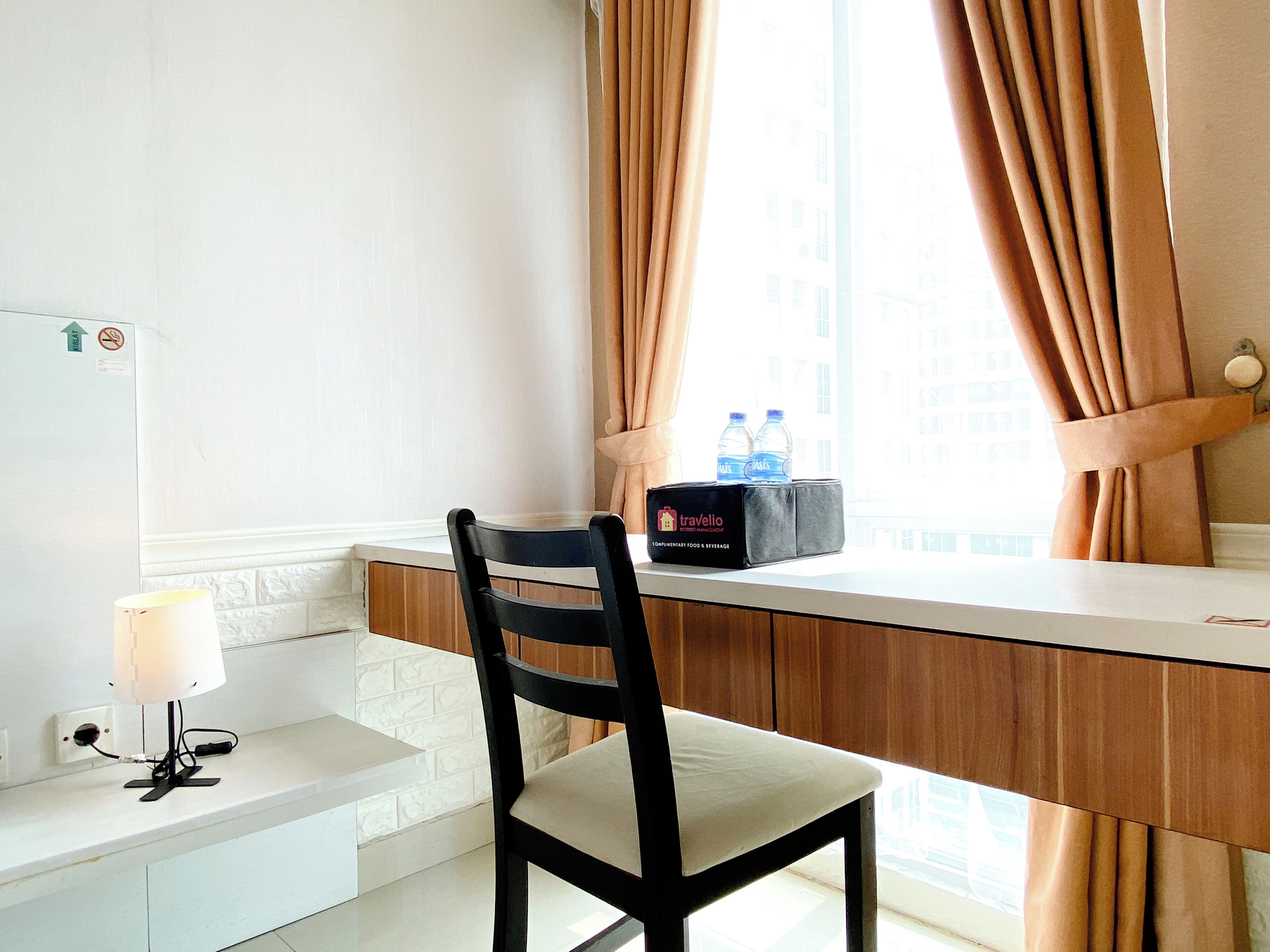 A hotel room with a desk, a chair, a lamp, a water bottle, and a travel bag.
