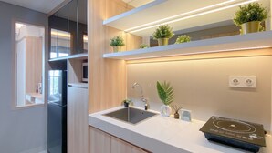 Cozinha moderna com frigorífico embutido, uma pia e bancada com fogão de indução integrado. Há plantas em vasos na bancada e um espelho acima da pia.