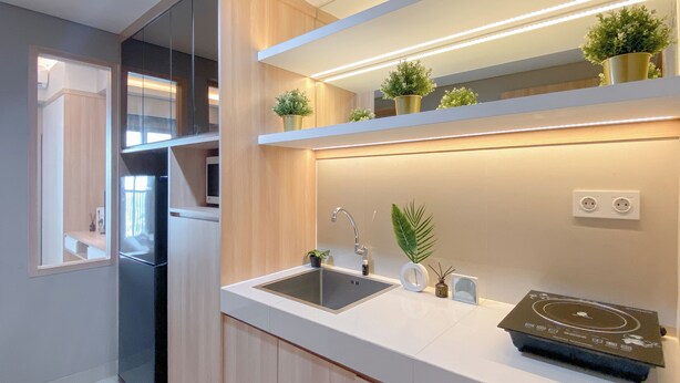 A modern kitchen with a built-in refrigerator, a sink, and a countertop with a built-in induction cooktop. There are potted plants on the countertop and a mirror above the sink.