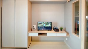 A modern room with a built-in TV, a white wardrobe, and a small plant on the desk.