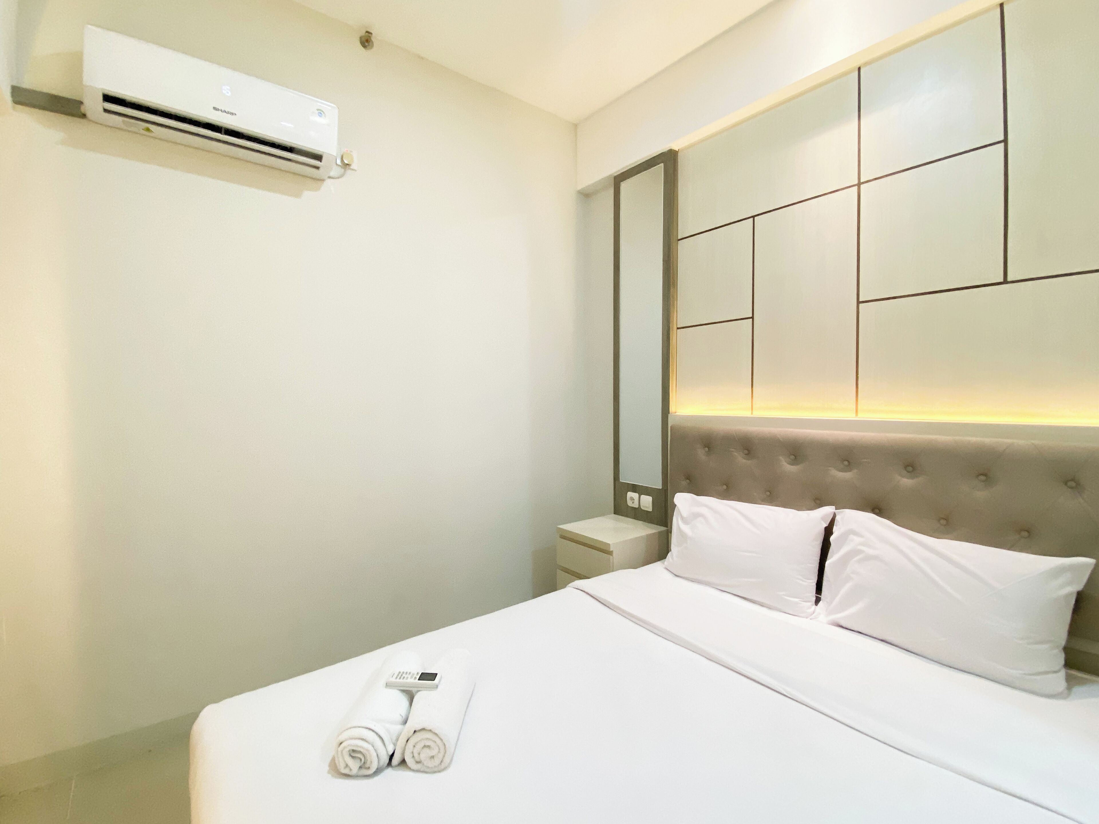 A hotel room with a bed, a bedside table, a mirror, and an air conditioning unit.