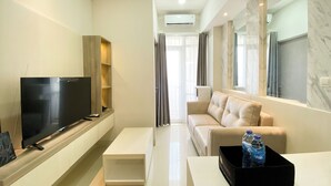 Ein modernes Wohnzimmer mit Flachbildfernseher, einer Couch, einem Couchtisch und einer schwarzen Ablage mit Wasserflaschen.