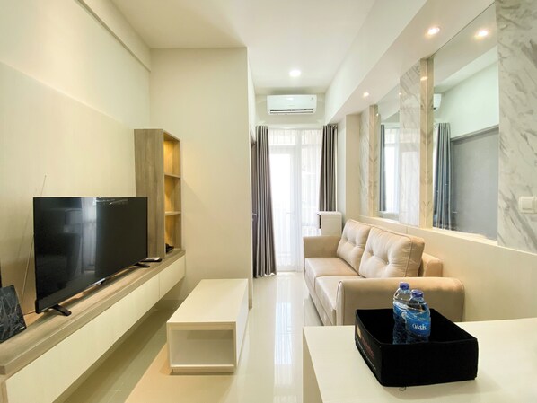 A modern living room with a flat-screen TV, a sofa, a coffee table, and a black tray with water bottles. - Spacious 2Br At Vasanta Innopark Apartment (Cikarang)