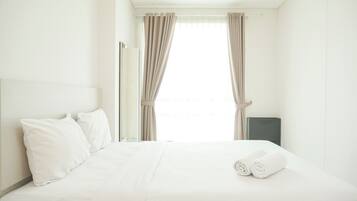 A hotel room with a neatly made bed, white linens, and a pair of rolled towels on the bed.