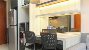 A compact kitchenette with a refrigerator, a sink, and a countertop. There are two black chairs and a small table. - Comfort And Cozy Living 1Br At Signature Park Grande Apartment (Jakarta)