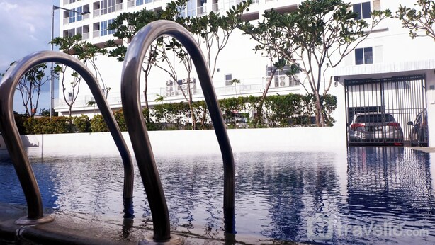 A swimming pool with metal railings, surrounded by trees and a white building in the background. - Good Deal And Homey 1Br Tifolia Apartment (Jakarta)