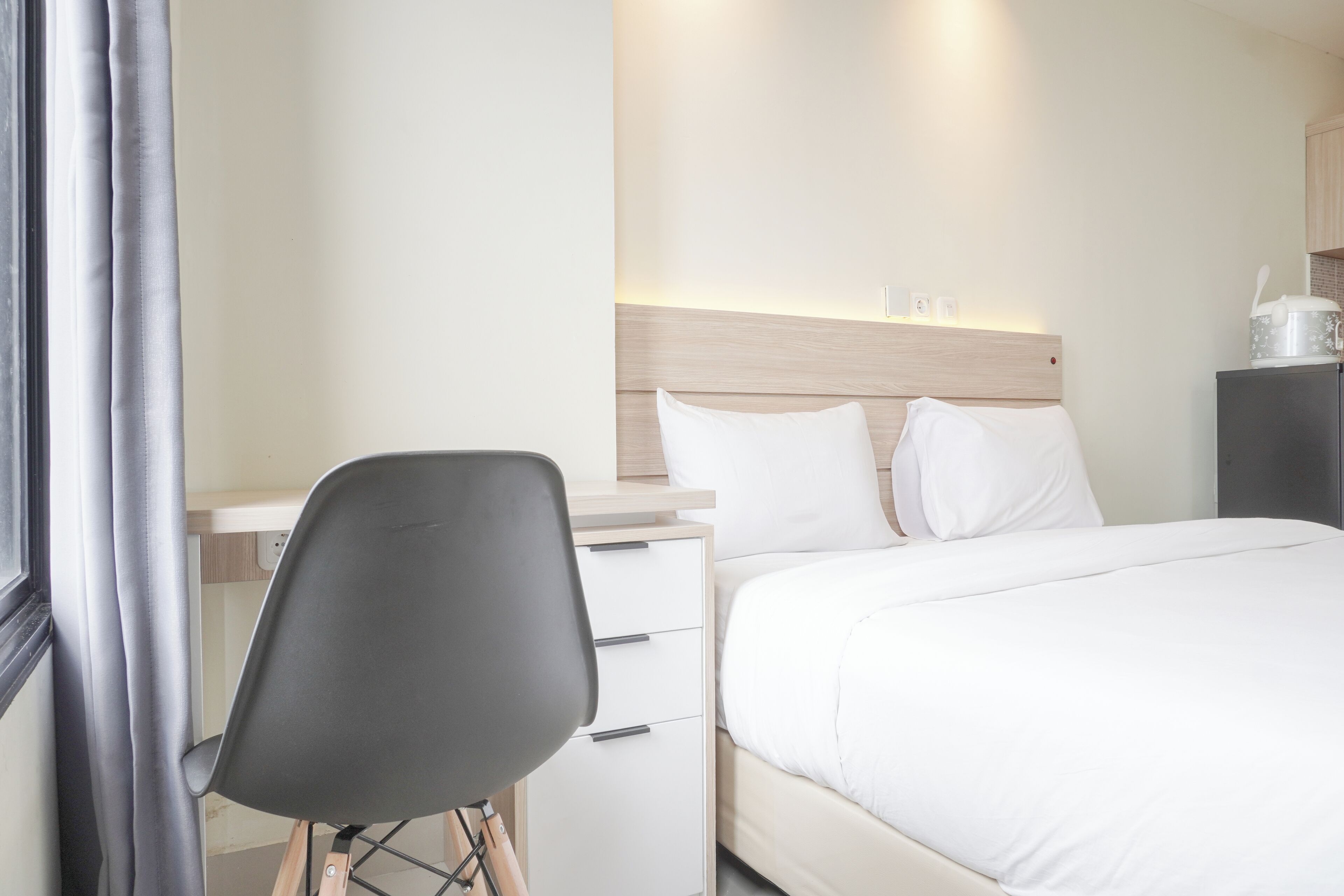 A hotel room with a bed, a desk with a chair, a nightstand, and a window with curtains.