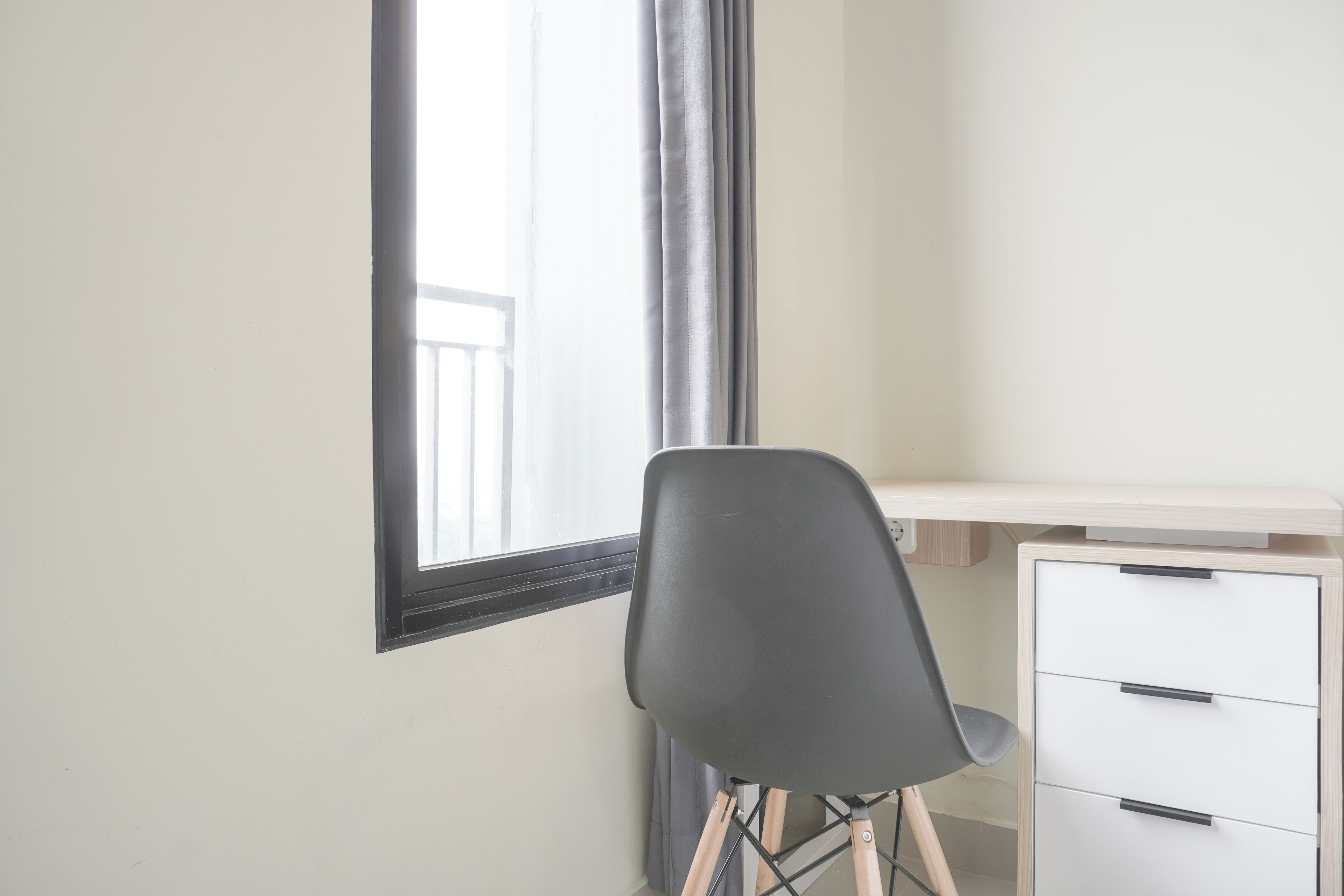 A room with a desk, chair, and a window with curtains.
