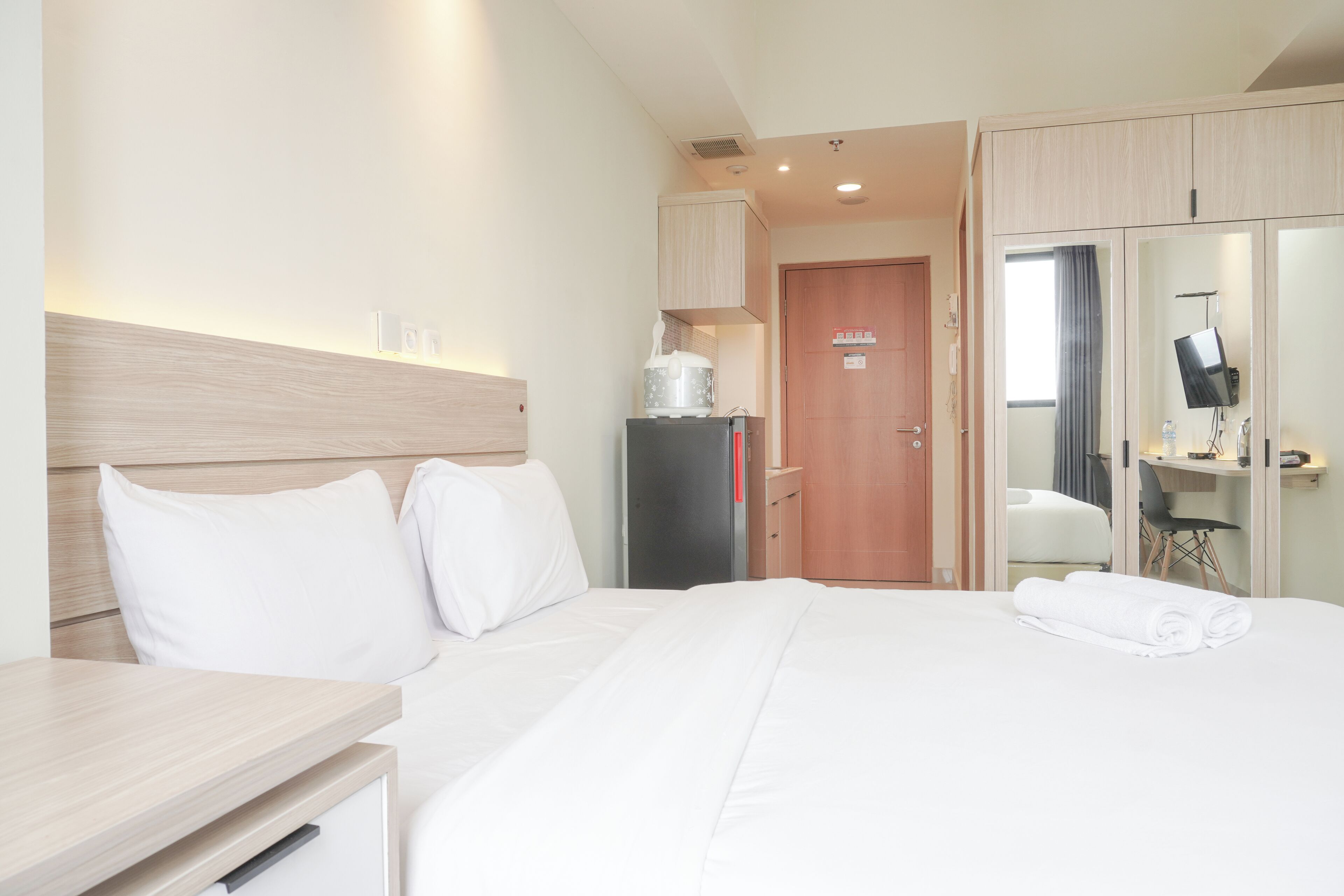 A hotel room with a bed, a desk, a wardrobe, and a mirror.