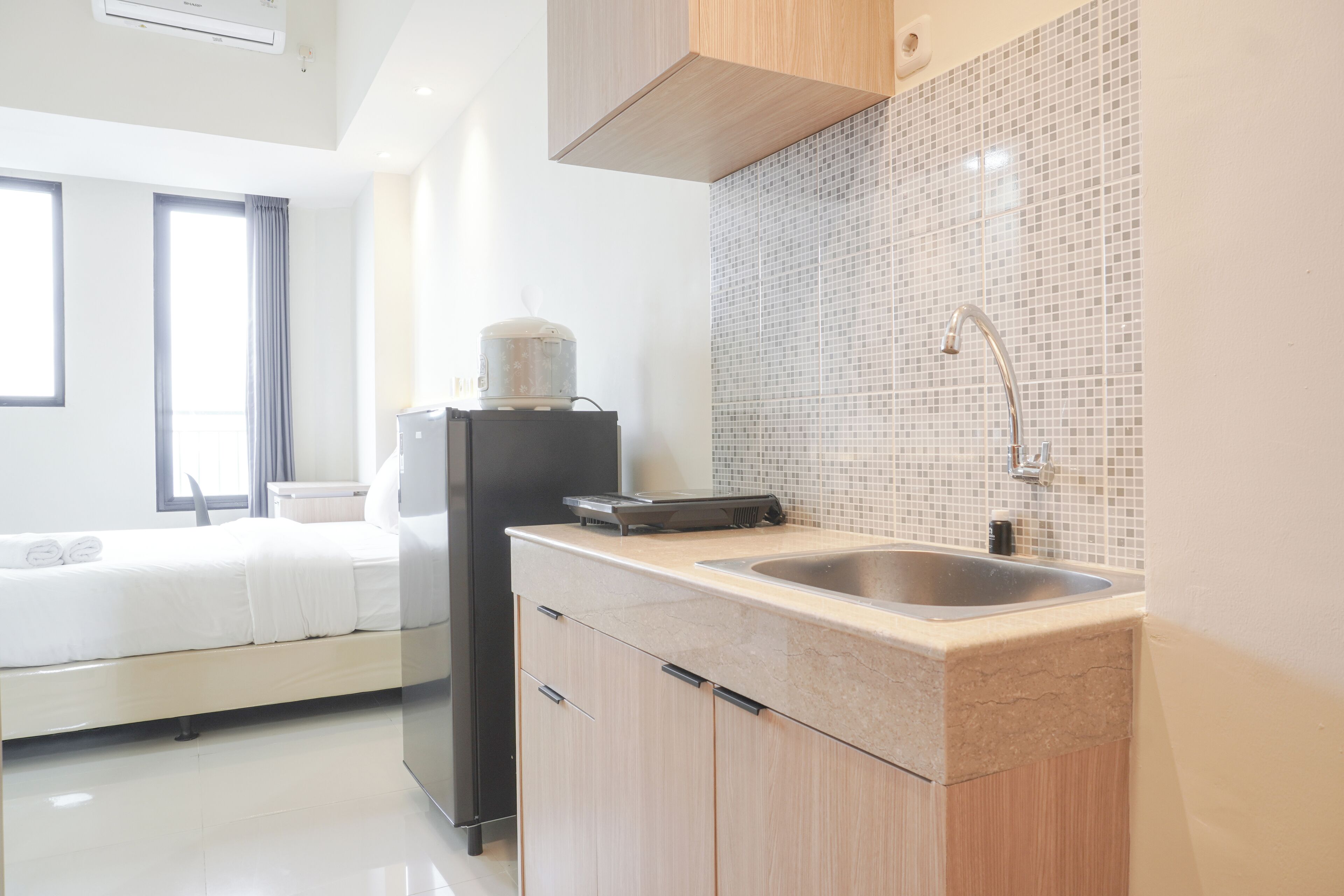 Una habitación de hotel moderna con kitchenette, una cama con ropa de cama blanca y un ventanal con cortinas.