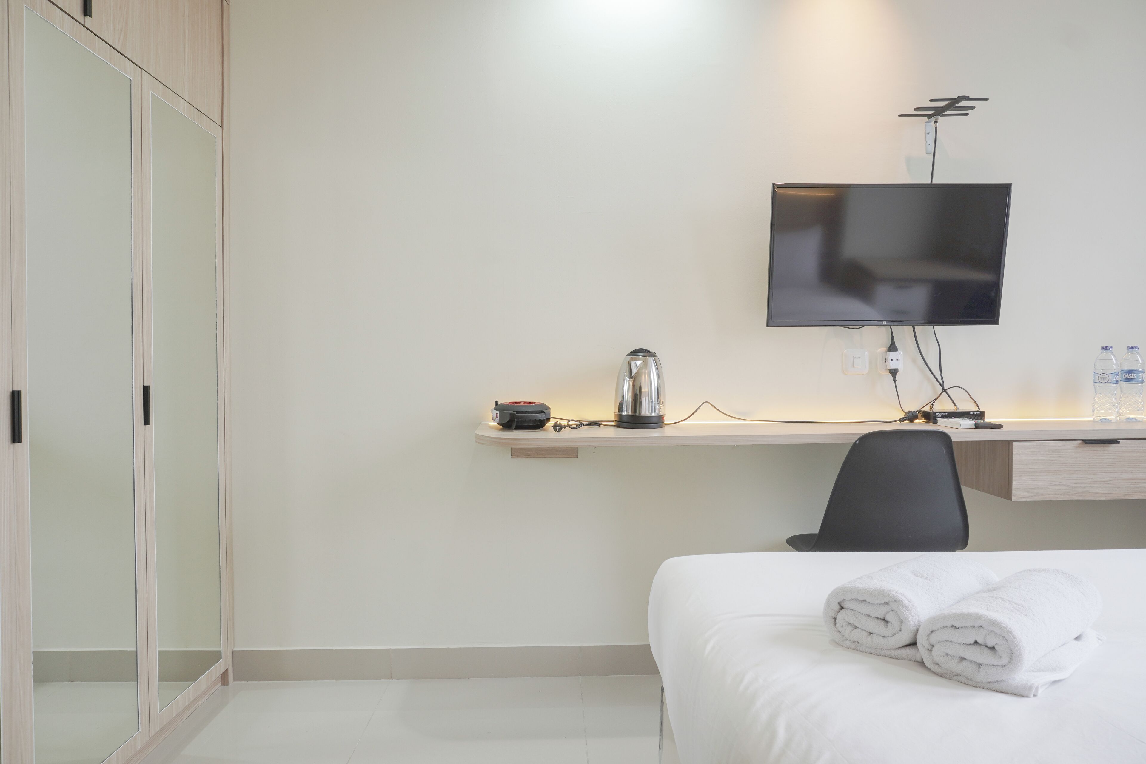 Ett hotellrum med en säng, ett skrivbord med en platt-TV, en vattenkokare och en stol.