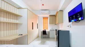A compact hotel room with a bed, a TV mounted on the wall, a small kitchenette, and a window with blinds. - Well Furnished And Cozy Studio Paltrow City Apartment (Semarang)