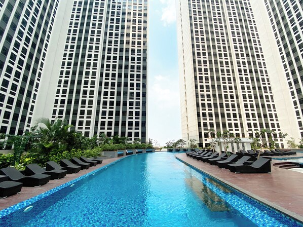 A swimming pool with lounge chairs and tall buildings in the background. - Best Deal And Comfy Studio Pollux Chadstone Apartment (Cikarang)