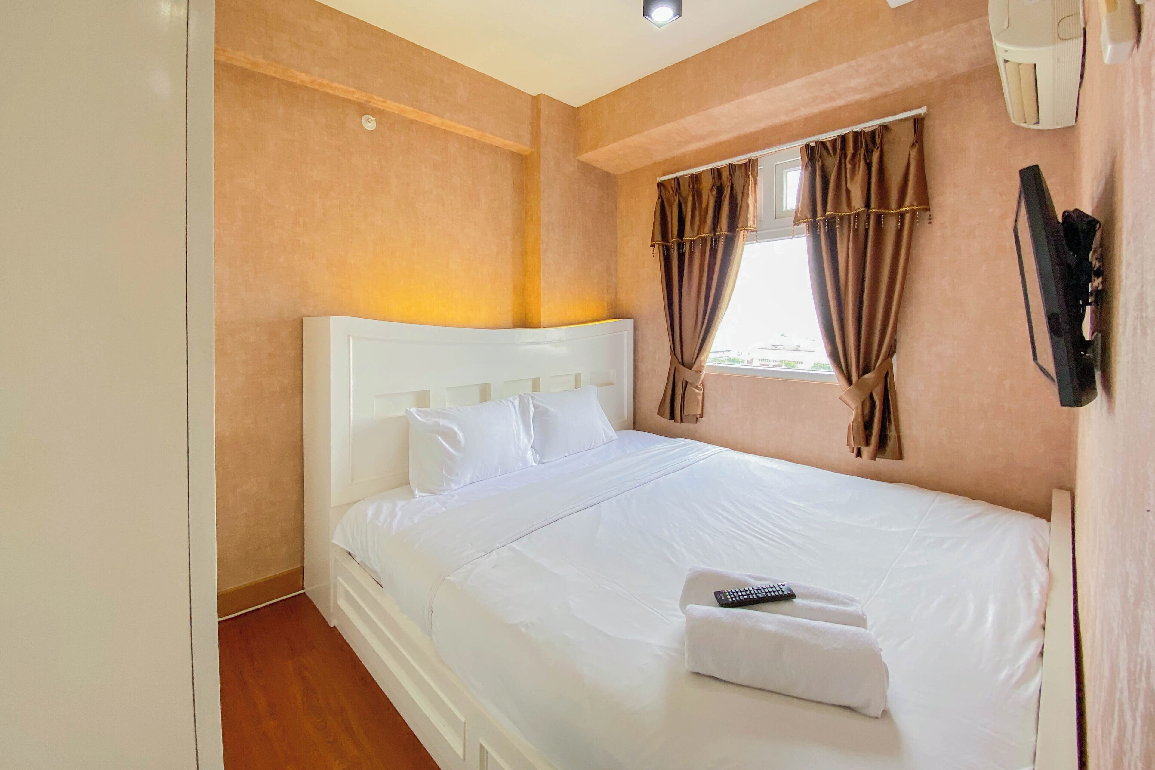 A hotel room with a single bed, white bedding, a remote control, and a window with curtains.