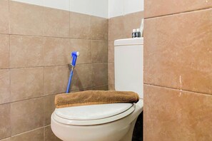 A bathroom with a toilet, a mop leaning against the wall, and a towel on the toilet seat.