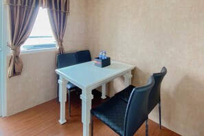 A room with a white table, two black chairs, a window with curtains, and a box with water bottles on the table.