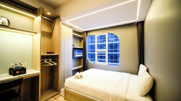 Une chambre d’hôtel moderne équipée d’un lit, d’un bureau, d’une armoire et d’une fenêtre donnant sur un paysage agréable.
