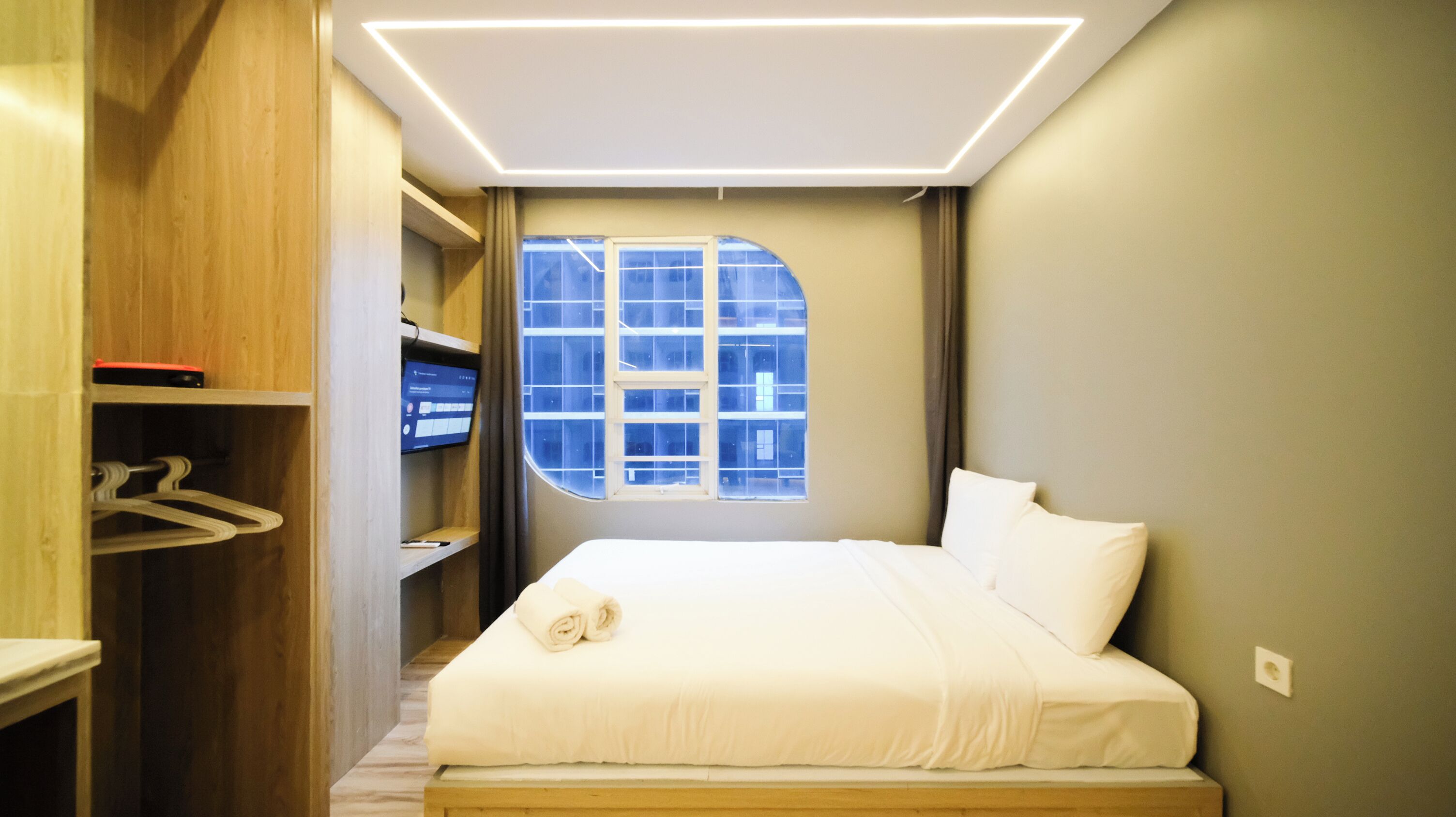 A hotel room with a bed, a wardrobe, a desk, and a window with a view of buildings.