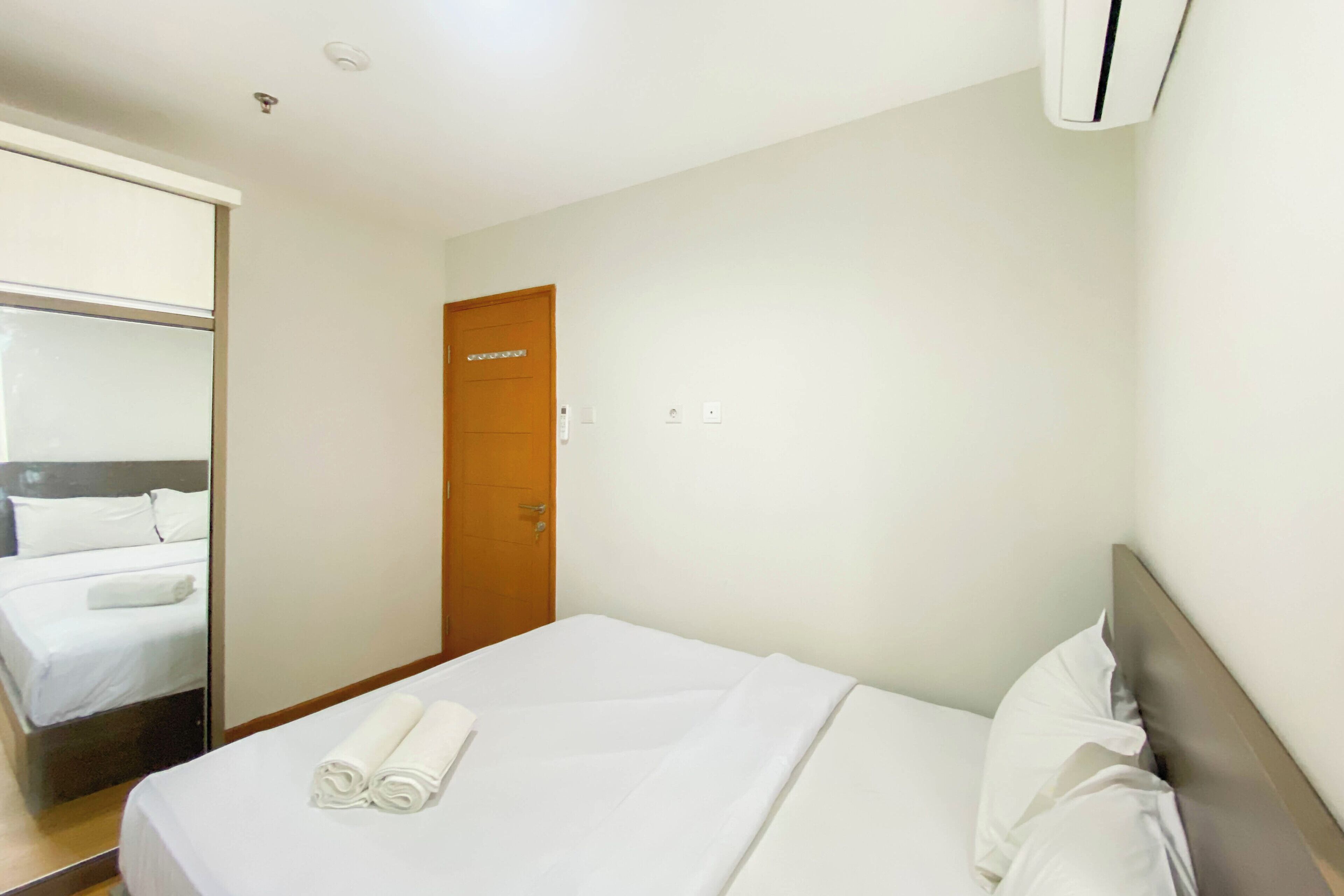 A hotel room with a bed, a wooden door, and an air conditioning unit.