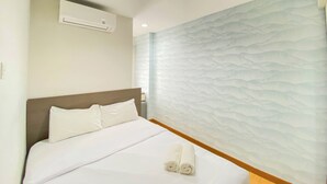 A hotel room with a bed, white linens, a wall-mounted air conditioner, and a textured wall design. - Comfort Living 2Br At Cinere Bellevue Suites Apartment (Depok)