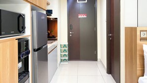 A compact kitchen with modern appliances, a door with a security lock, and a small countertop. - Minimalist Design Studio At Pollux Chadstone Apartment (Cikarang)