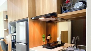 A compact kitchen with a built-in microwave, a stainless steel refrigerator, a sink with a modern faucet, and wooden cabinetry. - Minimalist Design Studio At Pollux Chadstone Apartment (Cikarang)
